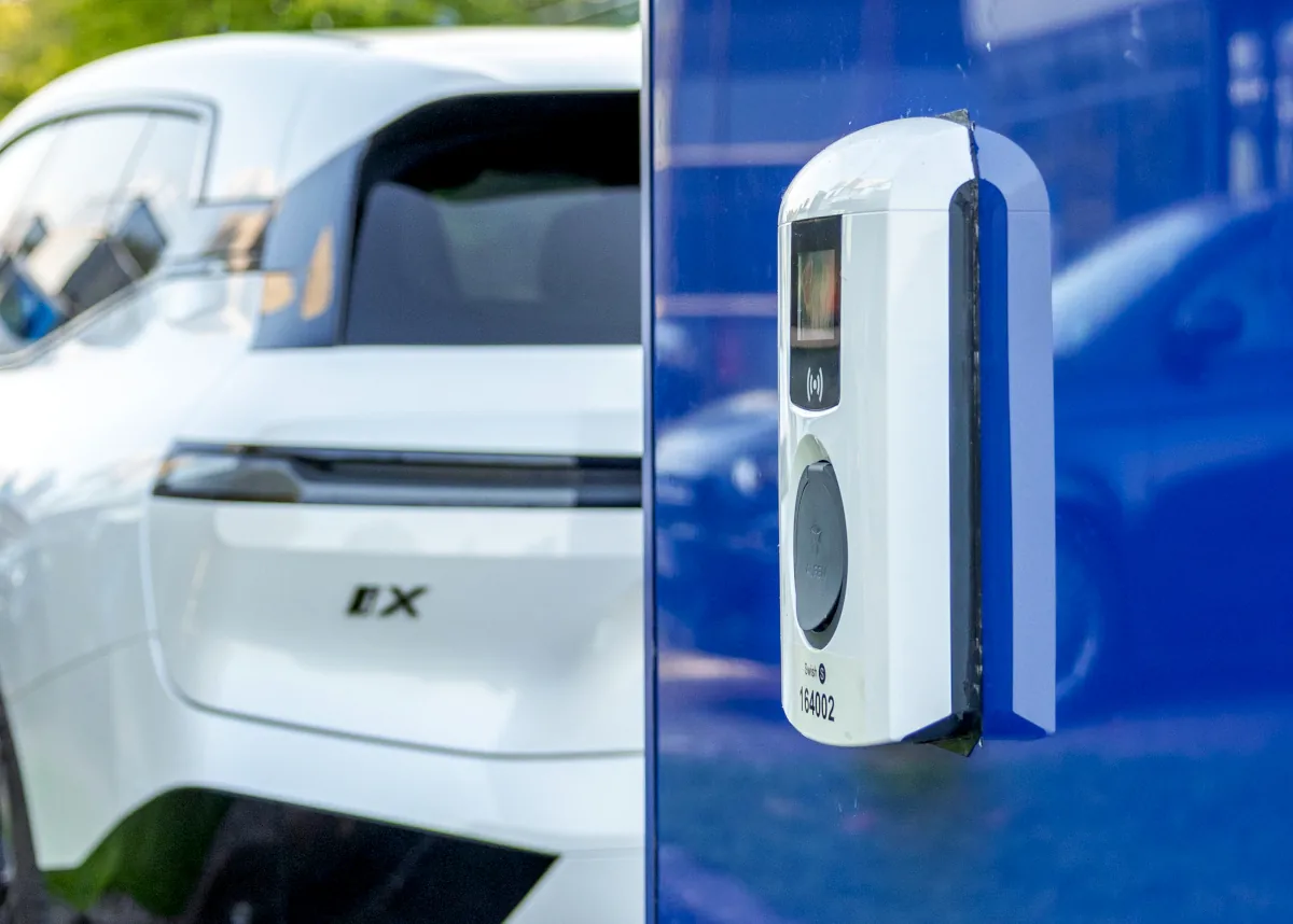 Primer plano de la estación de recarga móvil SwisHub, mostrando un cargador AC integrado con la parte trasera de un vehículo al fondo.